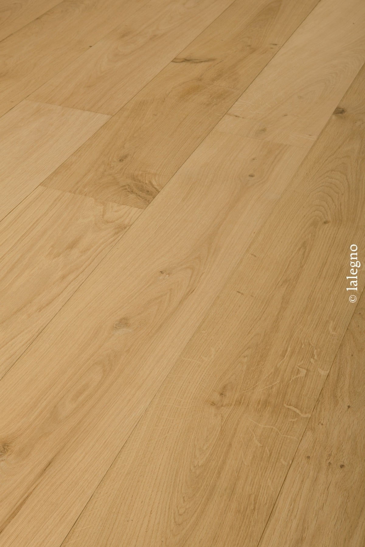 Plancher en chêne clair, finition naturelle, avec lames larges posées en diagonale. Détail du grain et des nœuds.