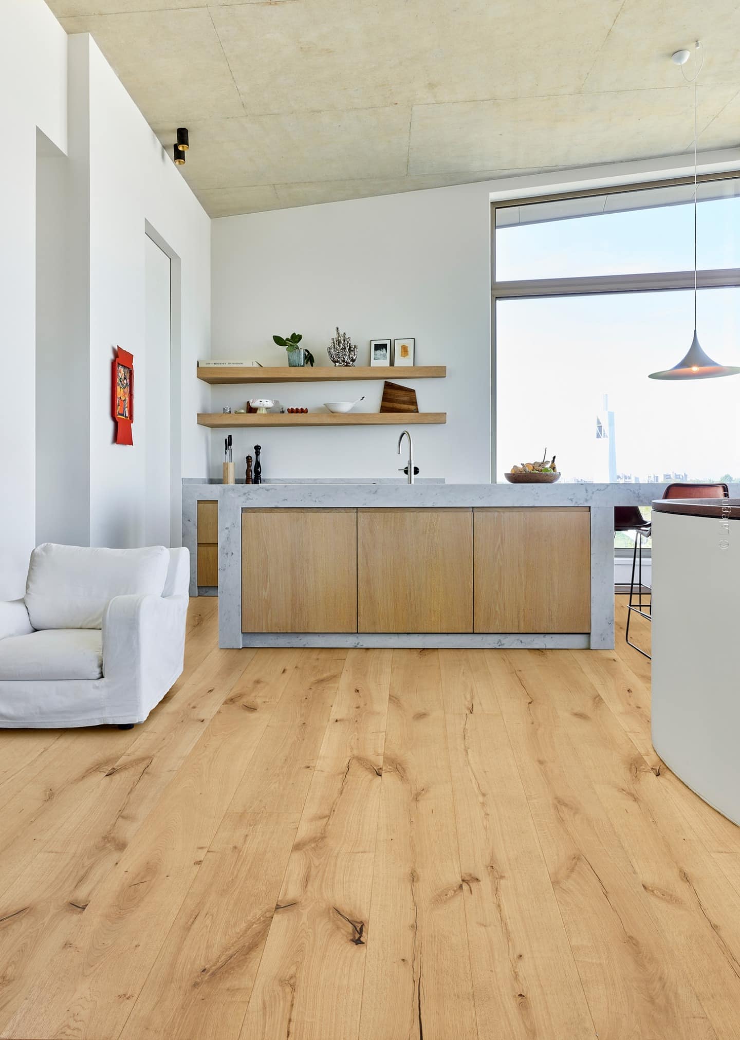 Intérieur moderne et lumineux. Plancher bois chêne rustique et nervuré contrastant avec l'îlot central en béton et les murs blancs.