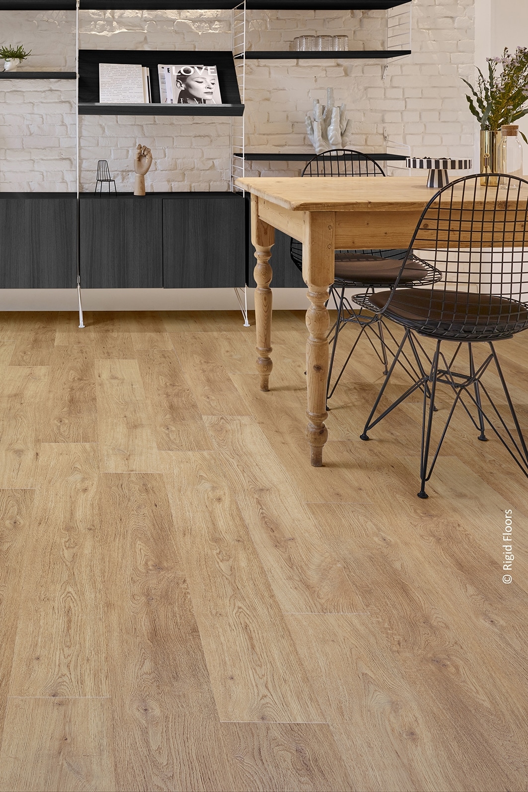 Plancher aspect bois clair dans une cuisine moderne. Table rustique, chaises filaires noires et mur en briques blanches.