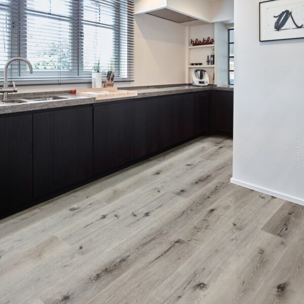 Cuisine moderne: armoires noires, comptoir gris, plancher aspect bois clair. Stores métalliques, évier inox et inscription "blabla".