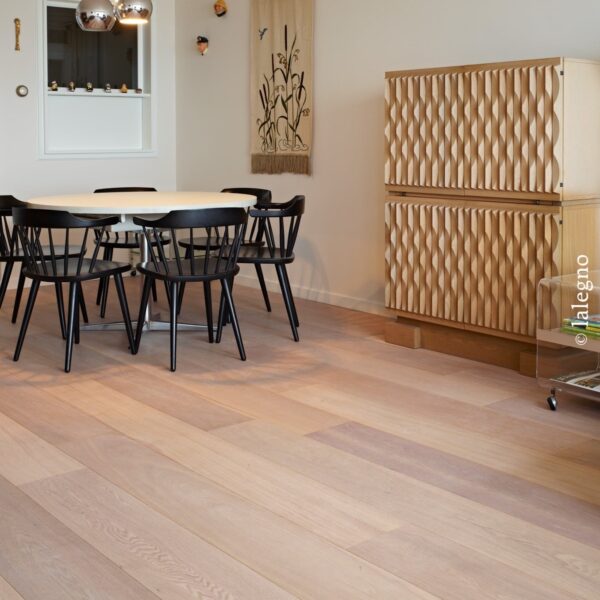 Ambiance lumineuse, plancher large latte chêne clair. Table ronde, chaises noires et buffet design aux portes en bois géométriques sculptées.