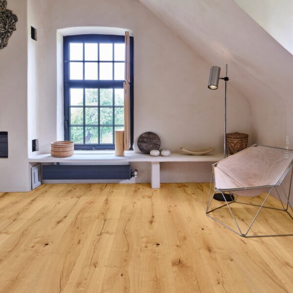 Plancher chêne rustique dans un intérieur mansardé aux murs clairs. Grande fenêtre noire et fauteuil papillon design sur poutre apparente.