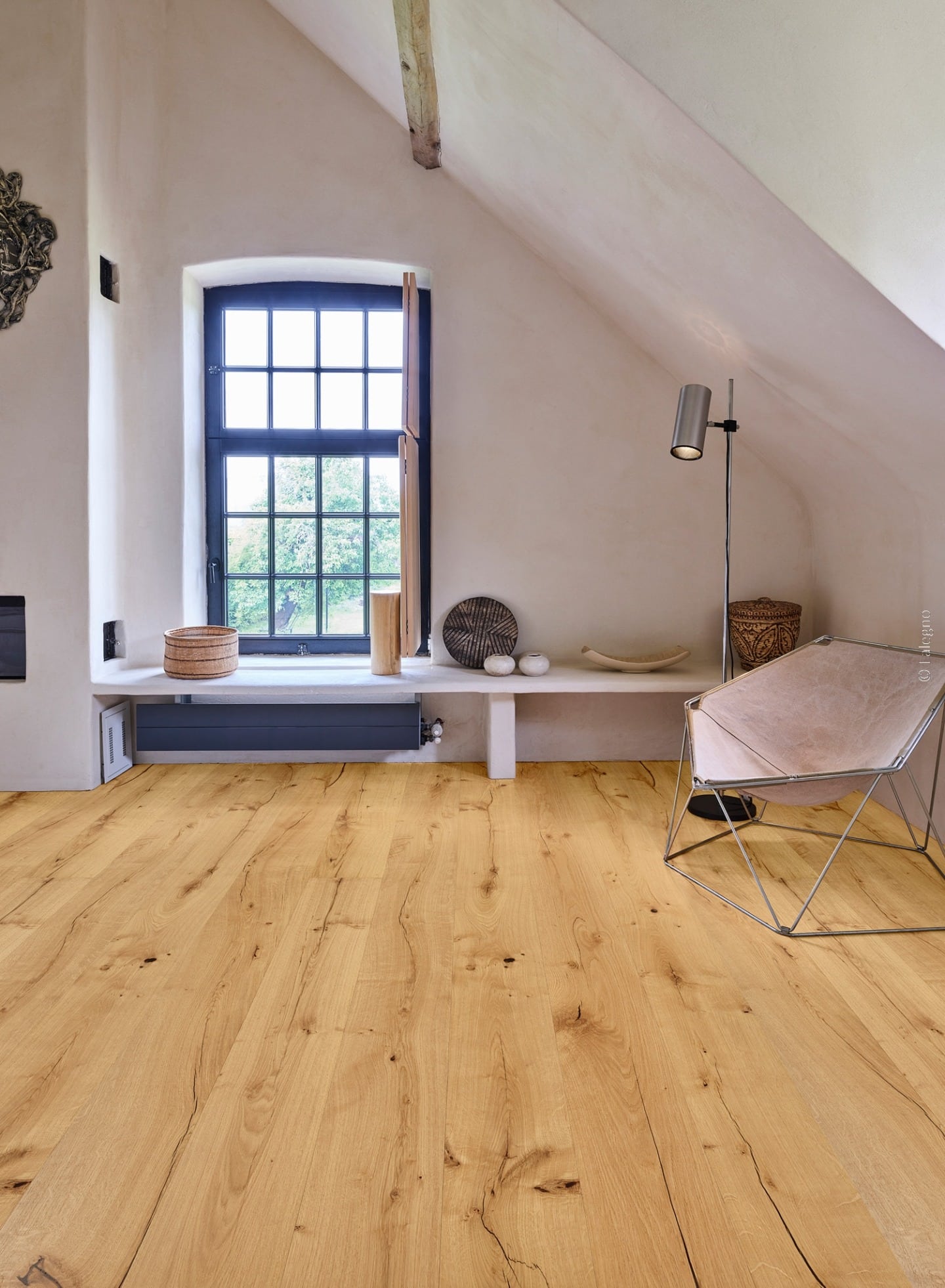 Plancher chêne rustique dans un intérieur mansardé aux murs clairs. Grande fenêtre noire et fauteuil papillon design sur poutre apparente.