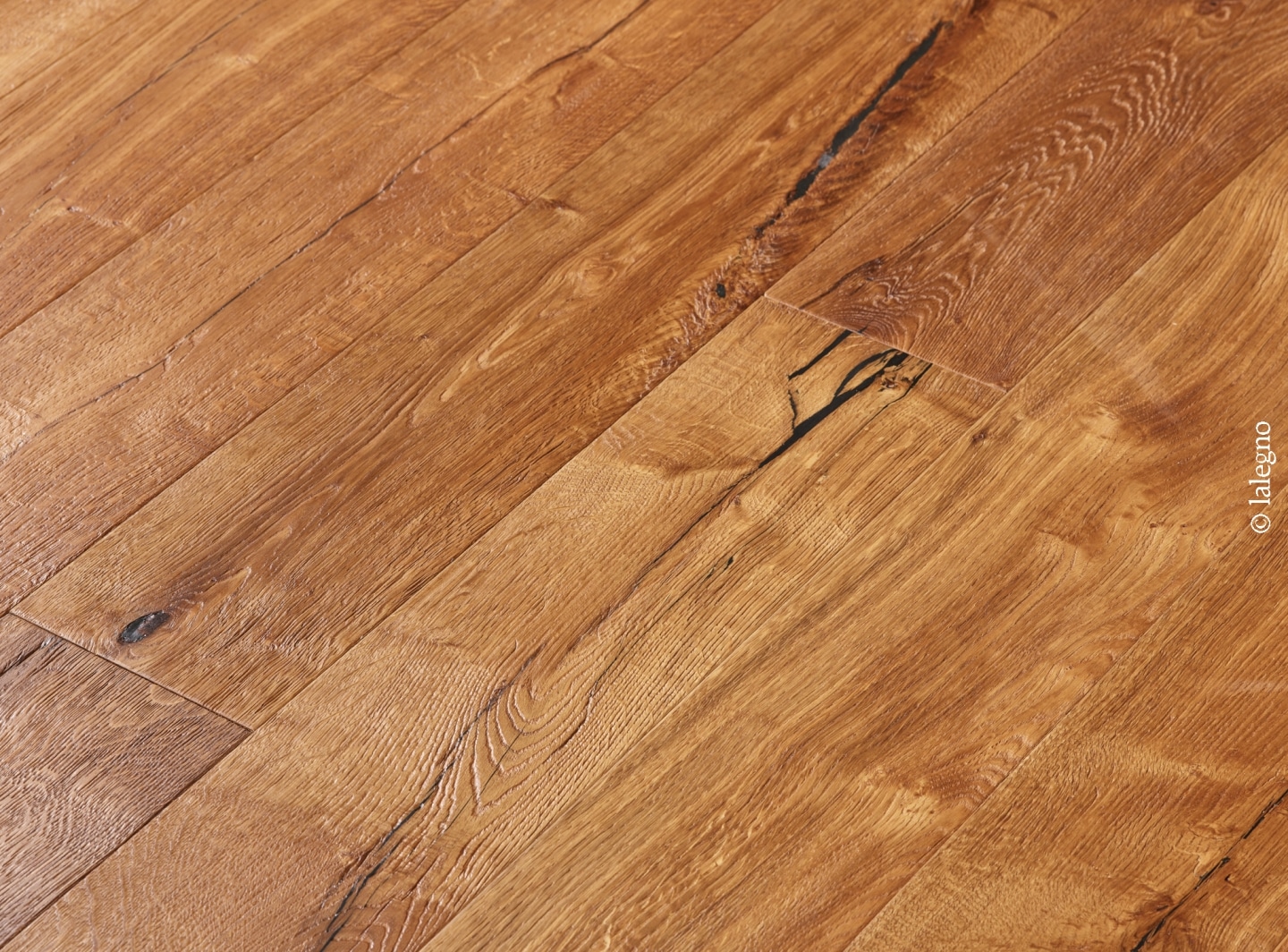 Gros plan sur un plancher en chêne rustique aux tons miel. Nœuds et fissures sombres apparents. Marque: © lalegno.