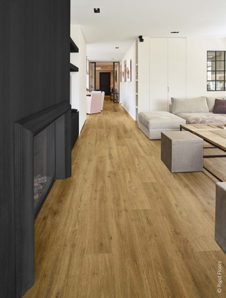 Plancher vinyle Rigid Floors chêne : ambiance chaleureuse Sol en vinyle Rigid Floors effet chêne doré dans un salon moderne. Cheminée noire contrastant avec les murs blancs et le canapé gris.
