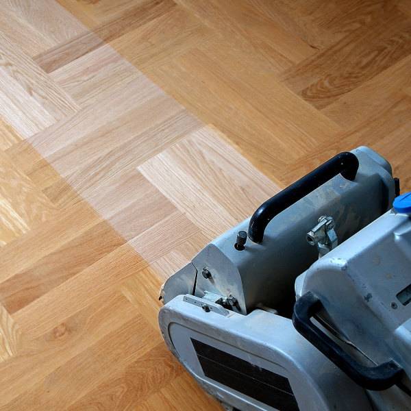 Ponçage de parquet : Rénover et restaurer un sol en chevrons. Ponceuse de parquet professionnelle sur sol en chêne chevrons. La machine a poncé une bande révélant le bois clair non traité.