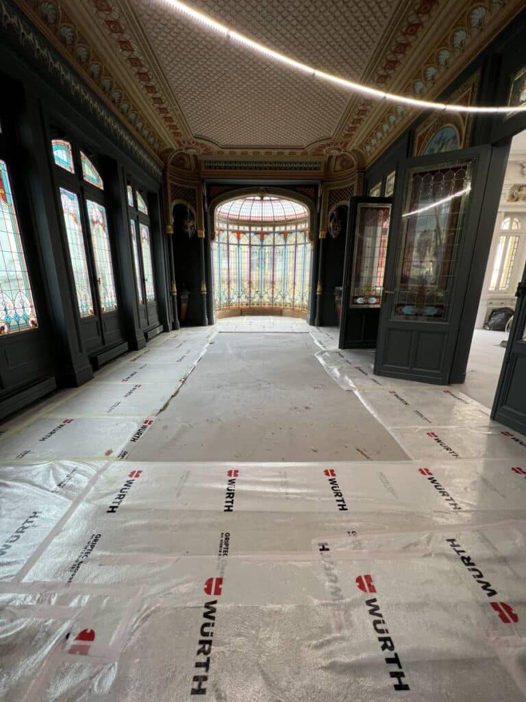 Rénovation Art Nouveau : galerie historique, vitraux et protection WURTH. Intérieur Art Nouveau en rénovation. Galerie avec vitraux, plafond orné et verrière. Sol protégé par des bâches WURTH.