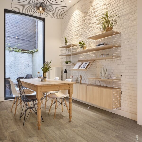 Salle à manger lumineuse avec sol vinyle aspect bois clair, mur de briques blanches texturées et étagères String. Table en bois rustique.