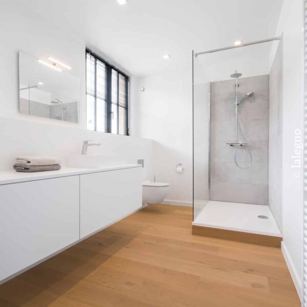 Salle de bain moderne minimaliste: plancher chêne clair, grande vanité blanche, douche italienne carrelée gris, fenêtre noire et lumières LED.