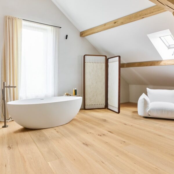 Luxueuse salle de bain sous-pente avec baignoire îlot blanche, parquet en chêne clair et charpente bois apparente.