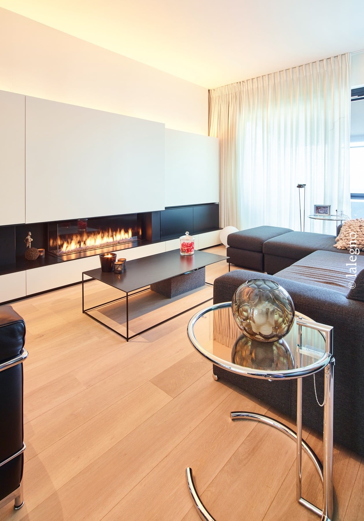 Salon minimaliste avec cheminée moderne horizontale et canapé gris sur plancher bois clair. Éclairage d'ambiance LED.