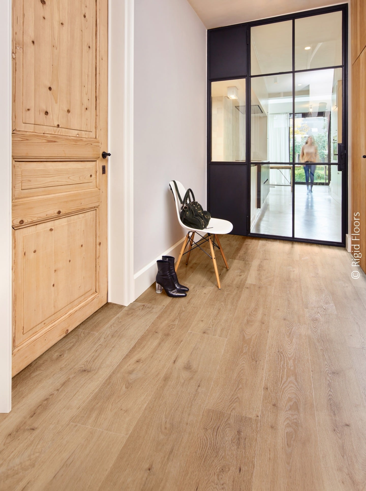 Entrée lumineuse avec sol effet bois clair, porte en pin rustique et verrière noire industrielle. Bottines noires sur le sol.