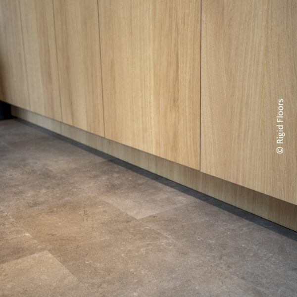 Carrelage vinyle rigide gris foncé effet pierre devant des armoires de cuisine sans poignée en chêne clair. (© Rigid Floors visible).