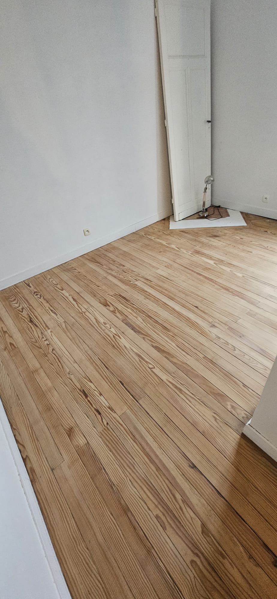 Parquet en bois clair aux veines marquées dans une pièce lumineuse aux murs blancs en cours de rénovation.