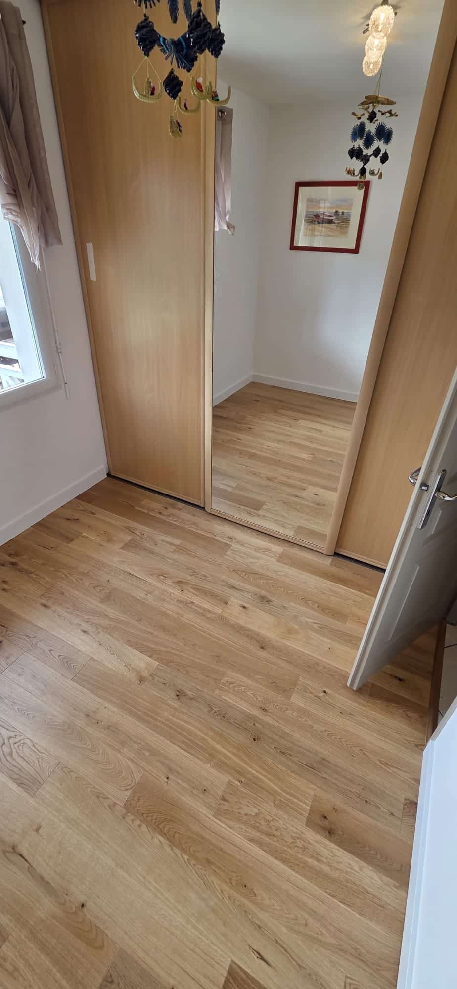 Parquet en chêne clair et placard avec porte miroir coulissante dans une chambre lumineuse et ordonnée.
