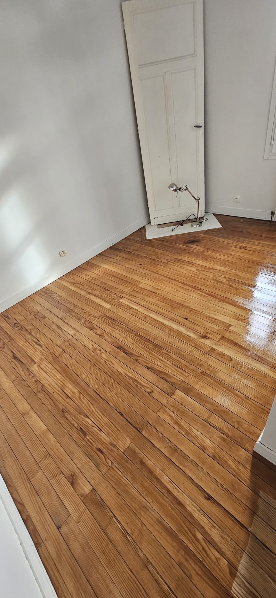 Parquet en chêne massif vitrifié et brillant dans une pièce lumineuse aux murs blancs.