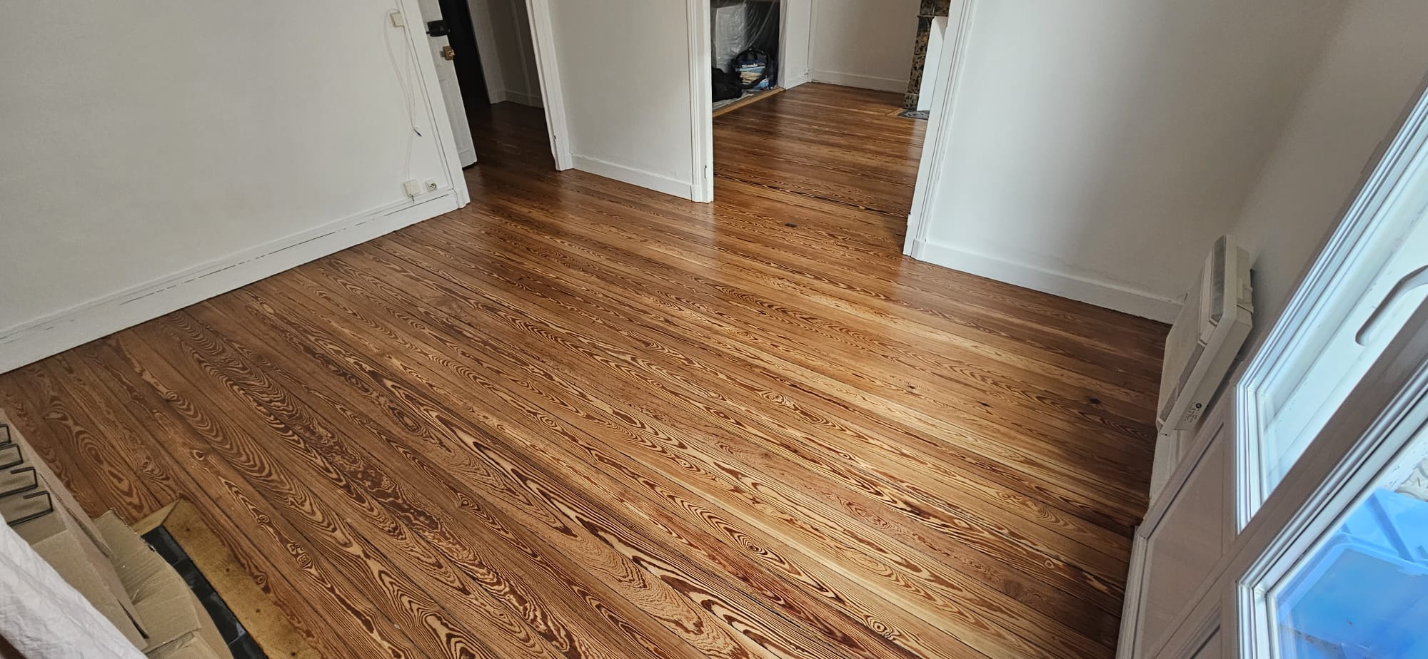 Parquet en pin massif aux veines sombres prononcées dans une pièce lumineuse aux murs et plinthes blancs.