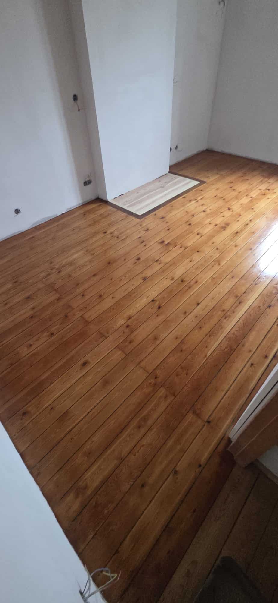 Plancher en bois massif vernis aux tons chauds dans une pièce lumineuse avec murs blancs.