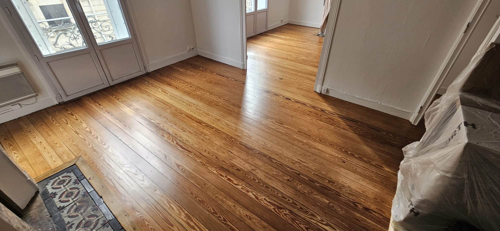 Parquet en bois de pin massif ciré dans un salon avec portes-fenêtres et carreaux de ciment décoratifs.