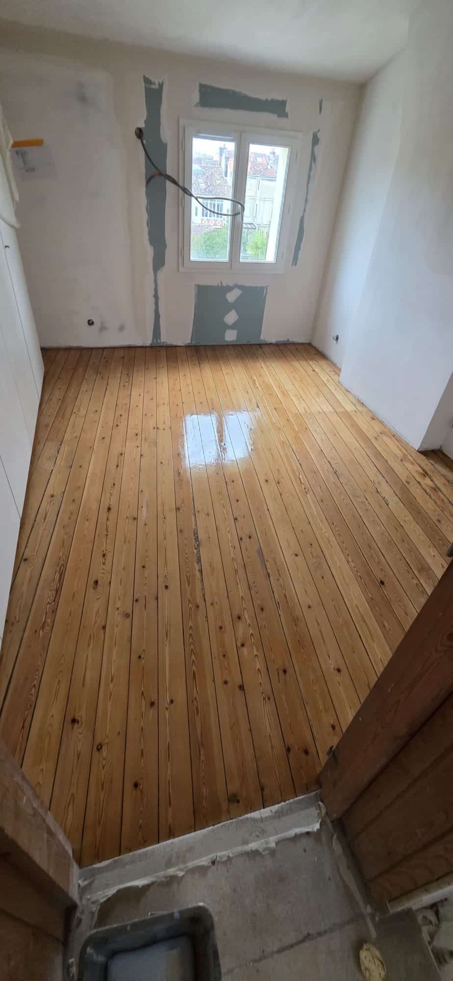 Sol en parquet massif brillant dans une chambre en cours de rénovation avec murs blancs et fenêtre.