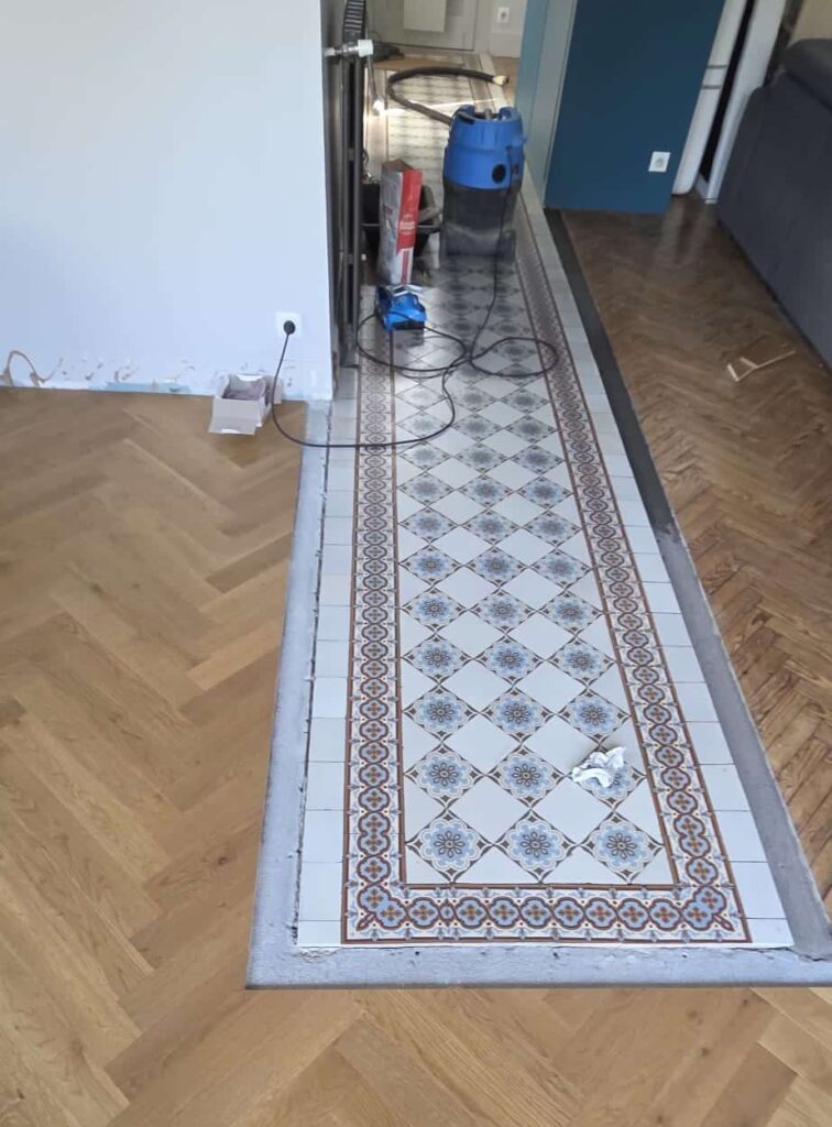 Parquet en chevrons entourant un tapis de carreaux de ciment à motifs bleus en cours de rénovation intérieure.