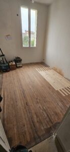Restauration d'un parquet ancien avec l'insertion de lames de bois neuf dans une chambre en rénovation.
