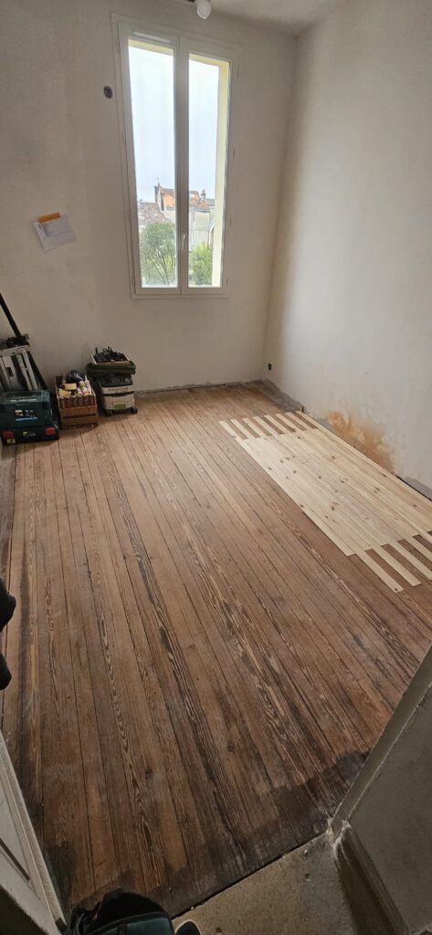 Restauration d'un parquet ancien avec l'insertion de lames de bois neuf dans une chambre en rénovation.