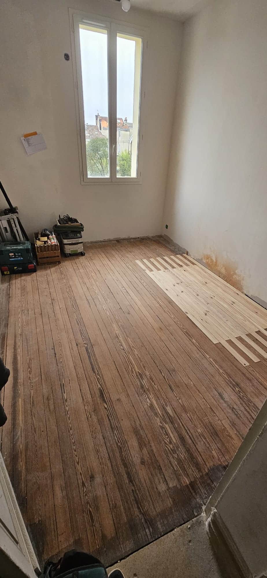 Restauration d'un parquet ancien avec l'insertion de lames de bois neuf dans une chambre en rénovation.
