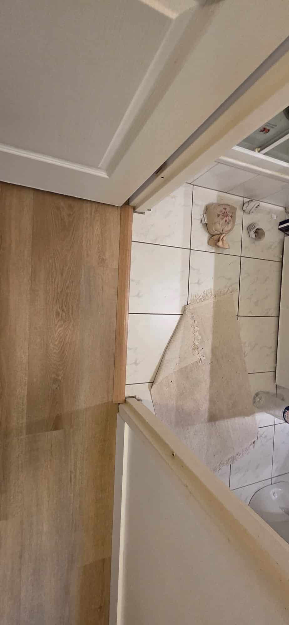 Seuil de porte en bois reliant un sol stratifié clair et le carrelage blanc d'une salle de bain.