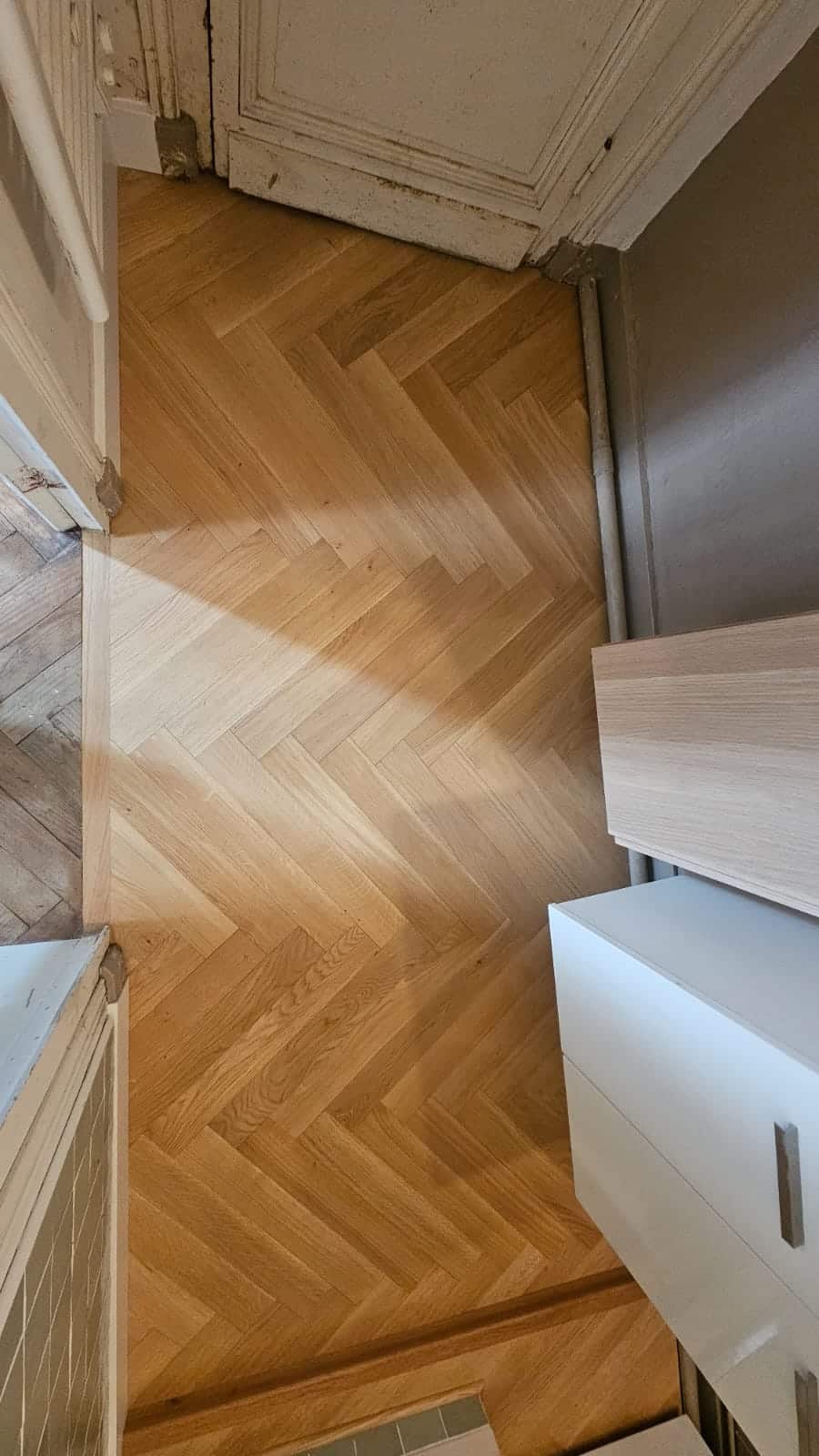 Sol en parquet de chêne clair à motif chevrons dans un couloir avec meuble blanc et bois.