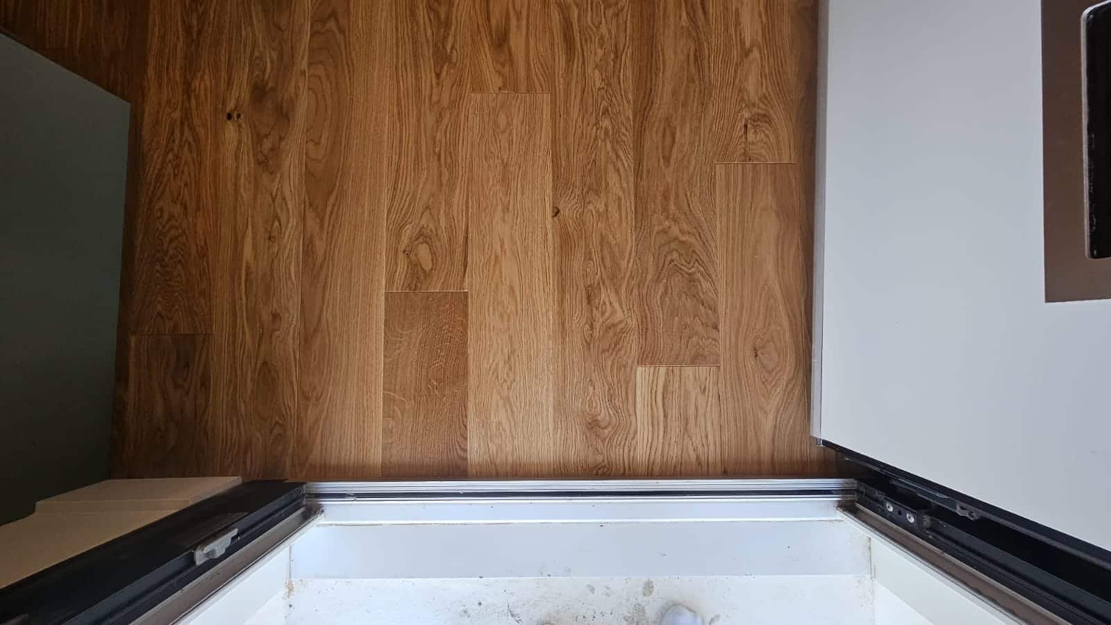 Parquet en chêne clair aux veines apparentes posé contre un seuil de porte blanc dans un intérieur moderne.