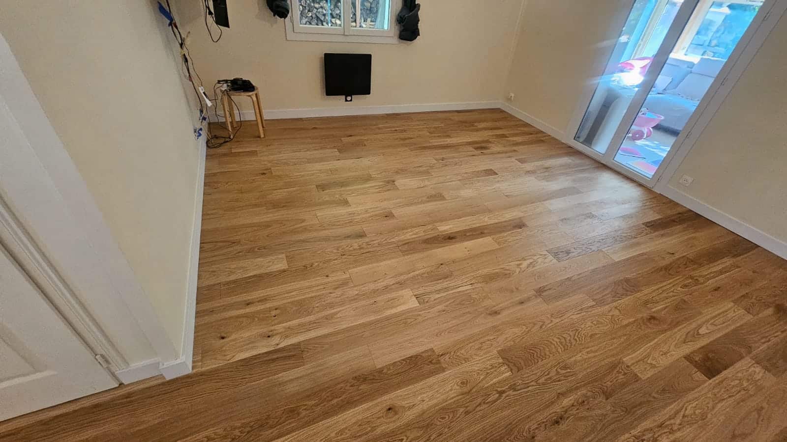 Parquet en bois de chêne clair posé dans une pièce lumineuse avec plinthes blanches et grandes baies vitrées.