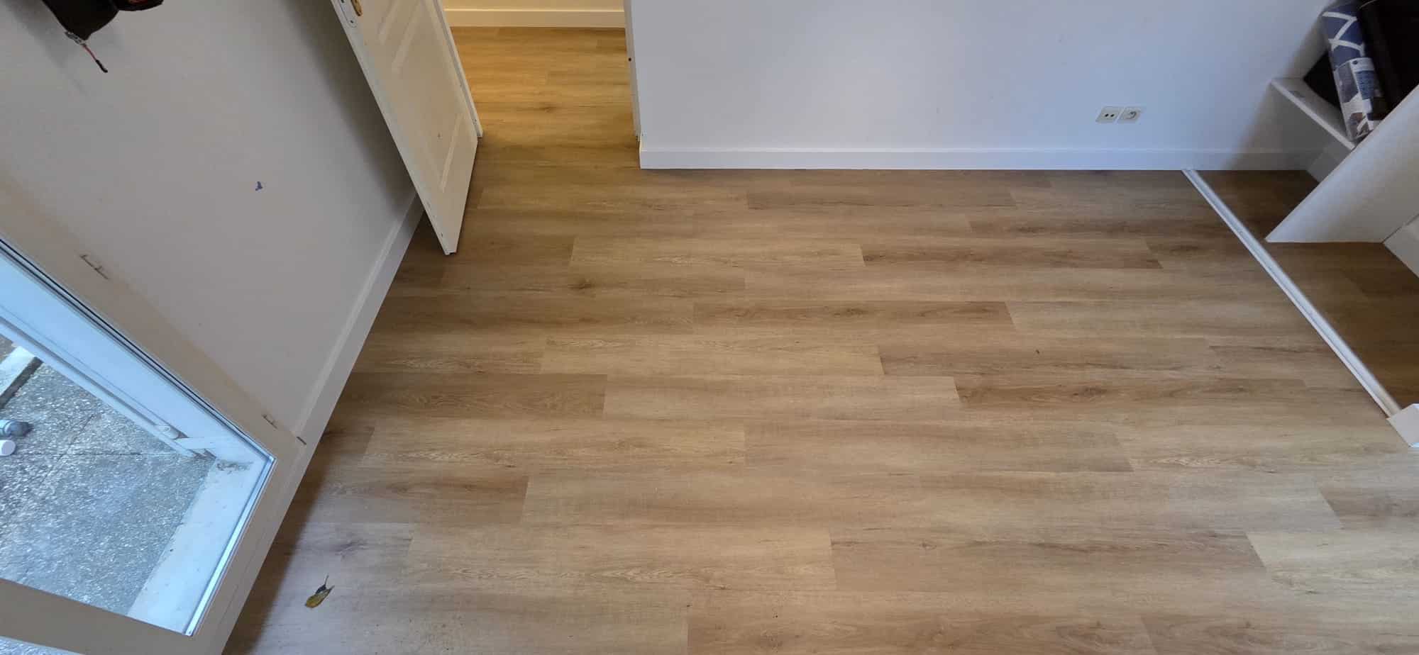 Parquet stratifié chêne clair dans une pièce moderne lumineuse avec murs blancs et plinthes assorties.