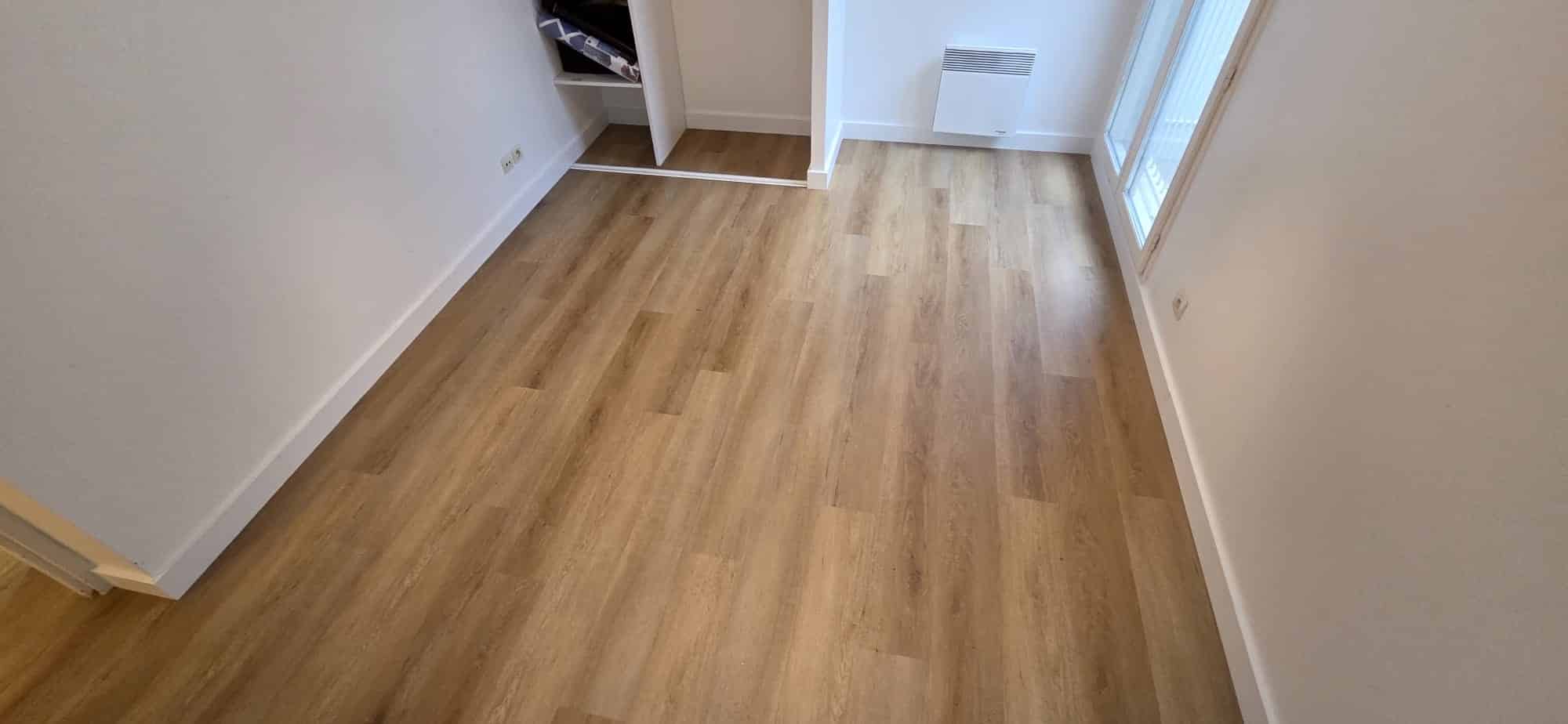 Chambre vide avec sol en parquet stratifié clair, murs blancs, radiateur mural et placard de rangement ouvert.