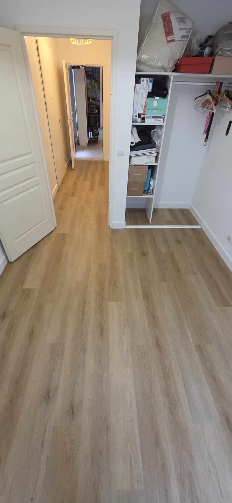 Sol stratifié chêne clair posé dans une chambre avec dressing ouvert et couloir en arrière-plan.
