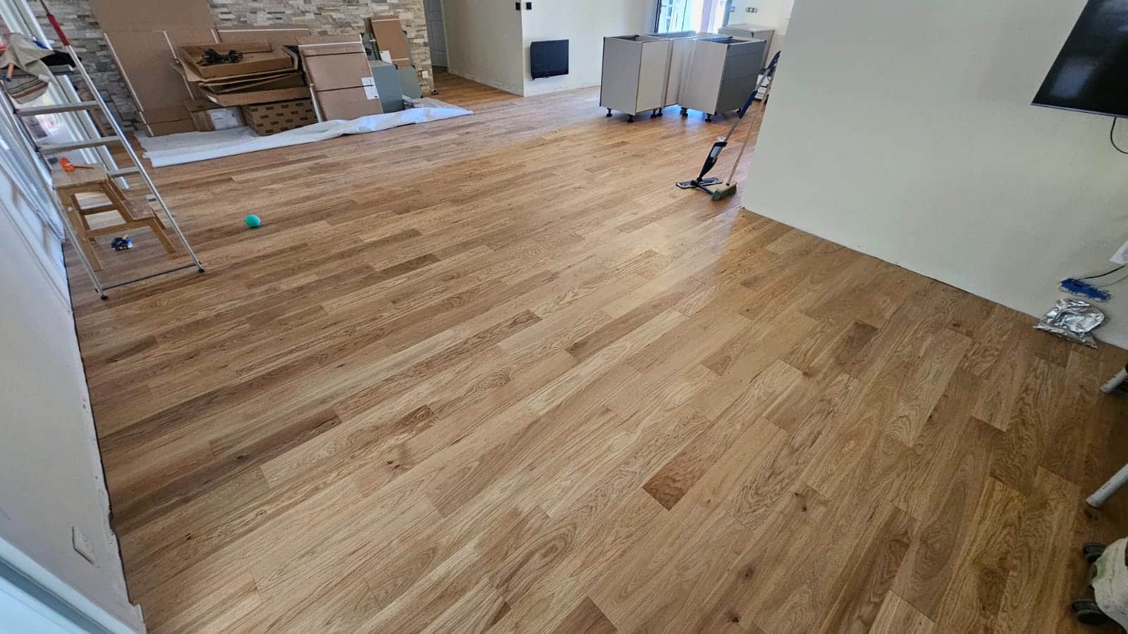 Parquet en chêne clair fraîchement posé dans une pièce en rénovation avec matériel de chantier et murs blancs.
