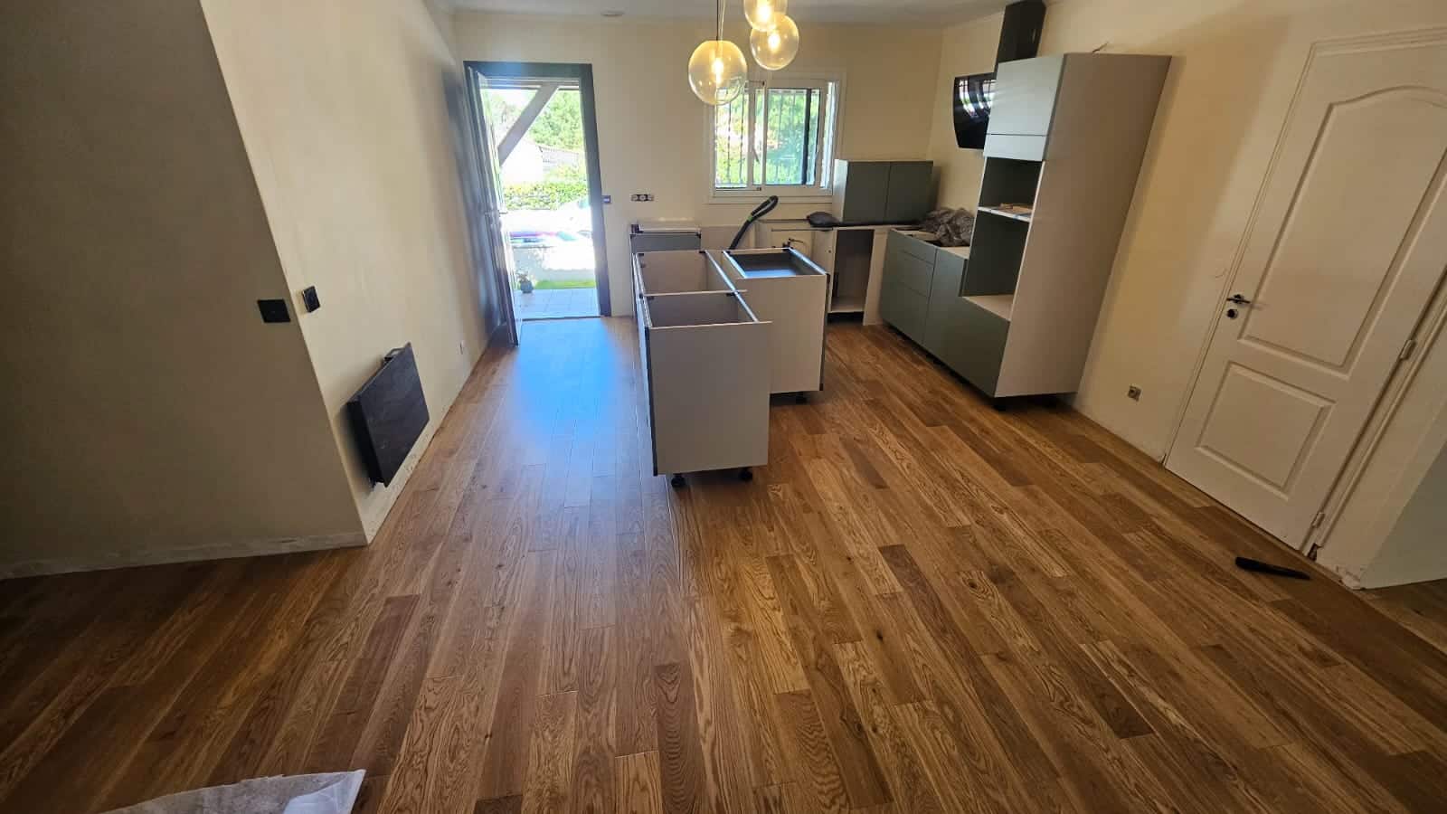 Installation d'une cuisine moderne avec îlot central et parquet en bois dans une pièce lumineuse en rénovation.