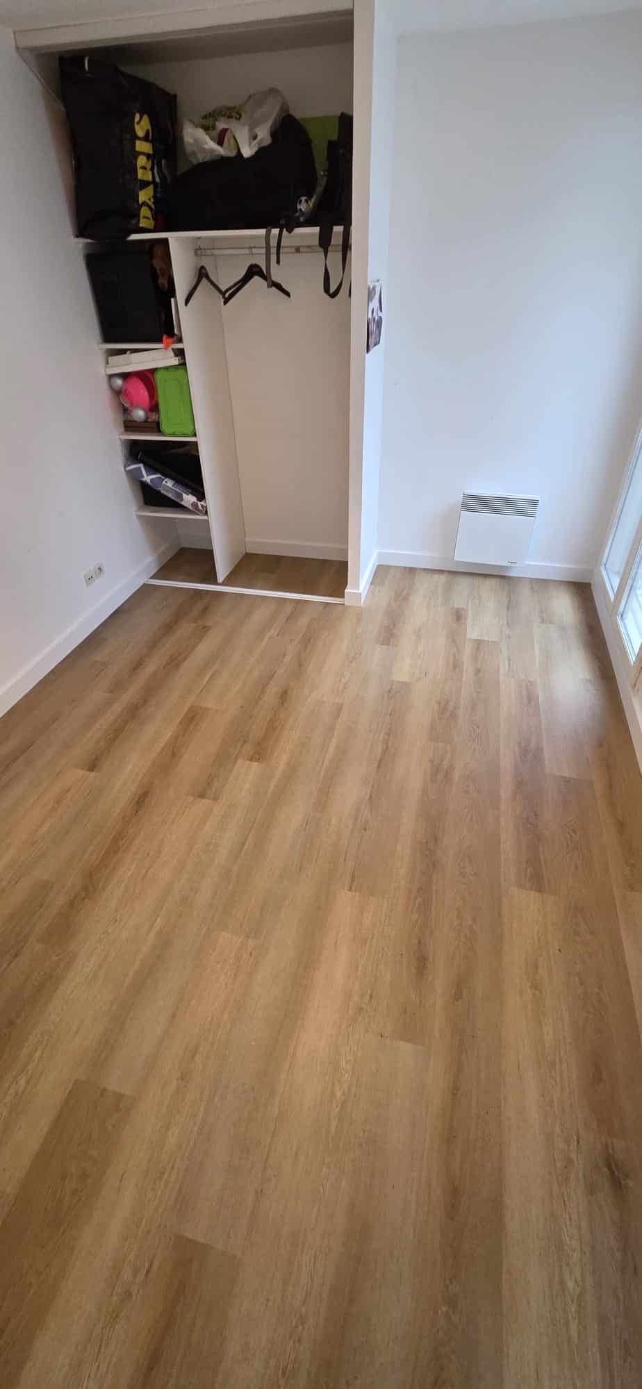 Chambre lumineuse avec sol en parquet bois clair, dressing ouvert et radiateur mural blanc sous une fenêtre.