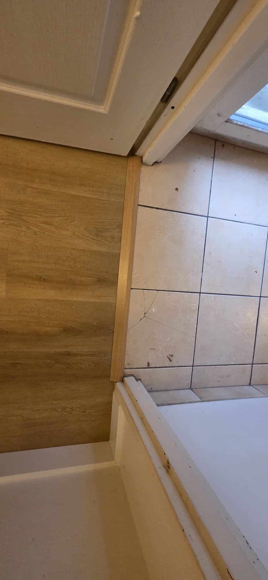 Seuil de transition entre parquet stratifié et carrelage beige à côté d'un bac de douche blanc.