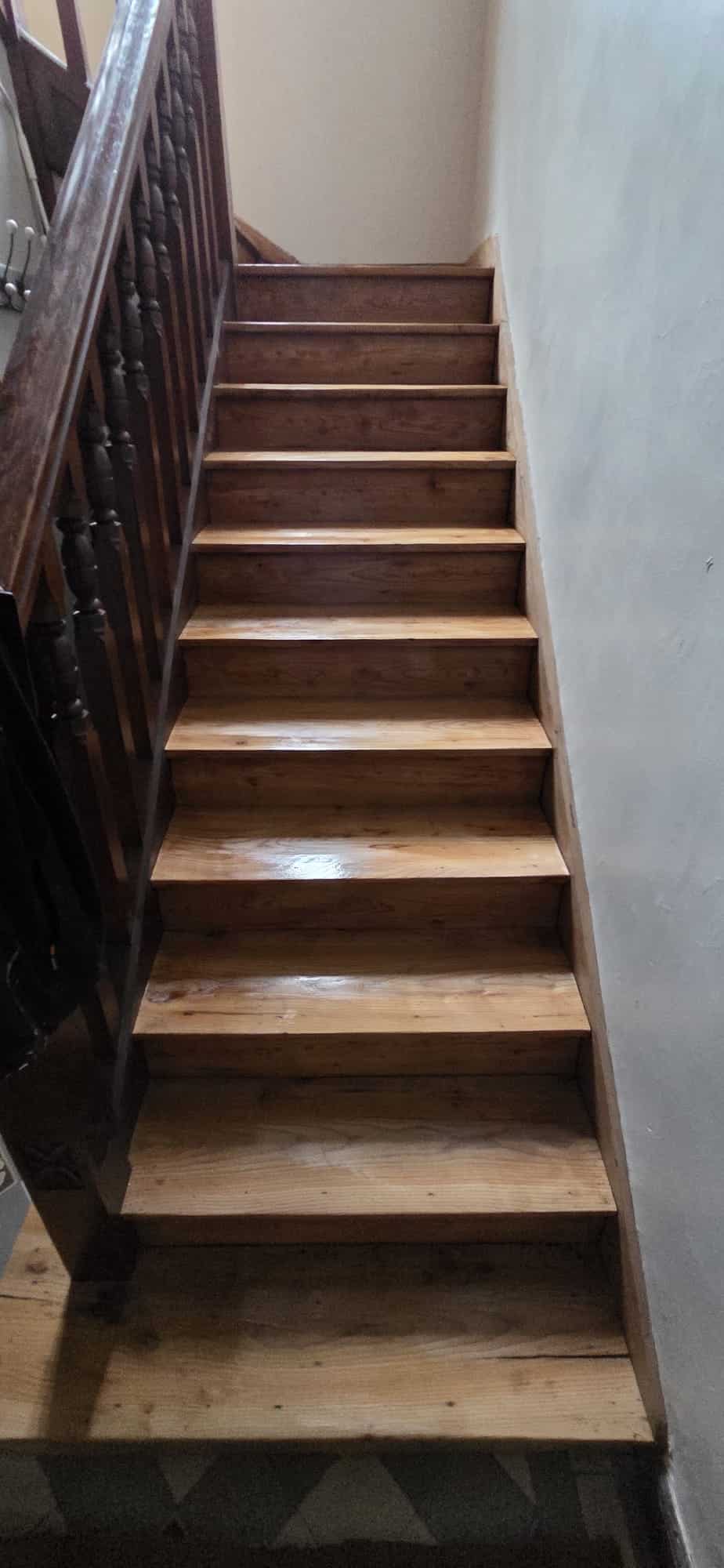 Escalier intérieur en bois verni avec rampe à balustres tournés, longeant un mur blanc épuré.