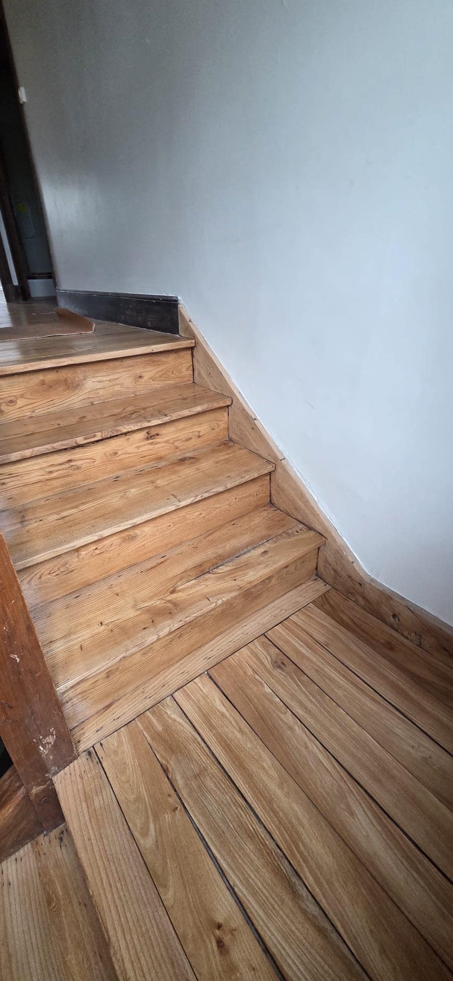 Escalier intérieur en bois de chêne massif et parquet rustique dans une maison aux murs blancs.