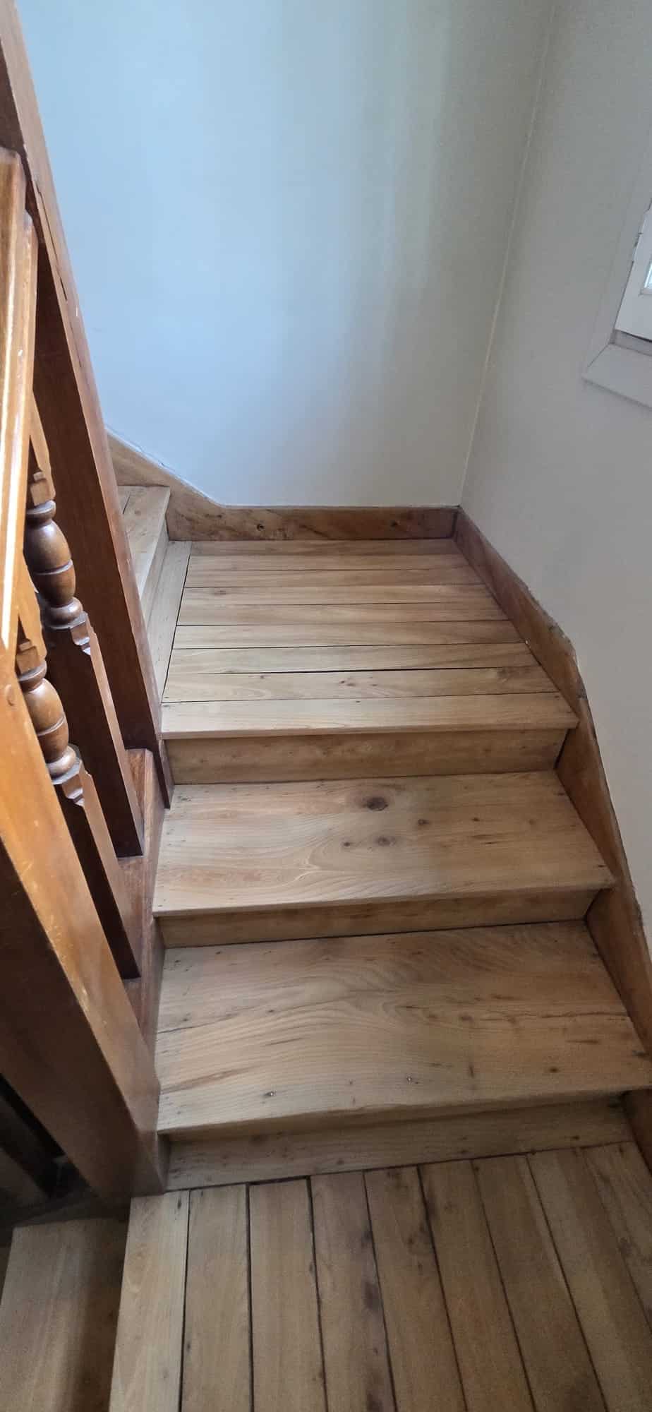 Escalier et palier en bois de pin clair avec garde-corps sculpté et murs blancs dans un intérieur rustique.