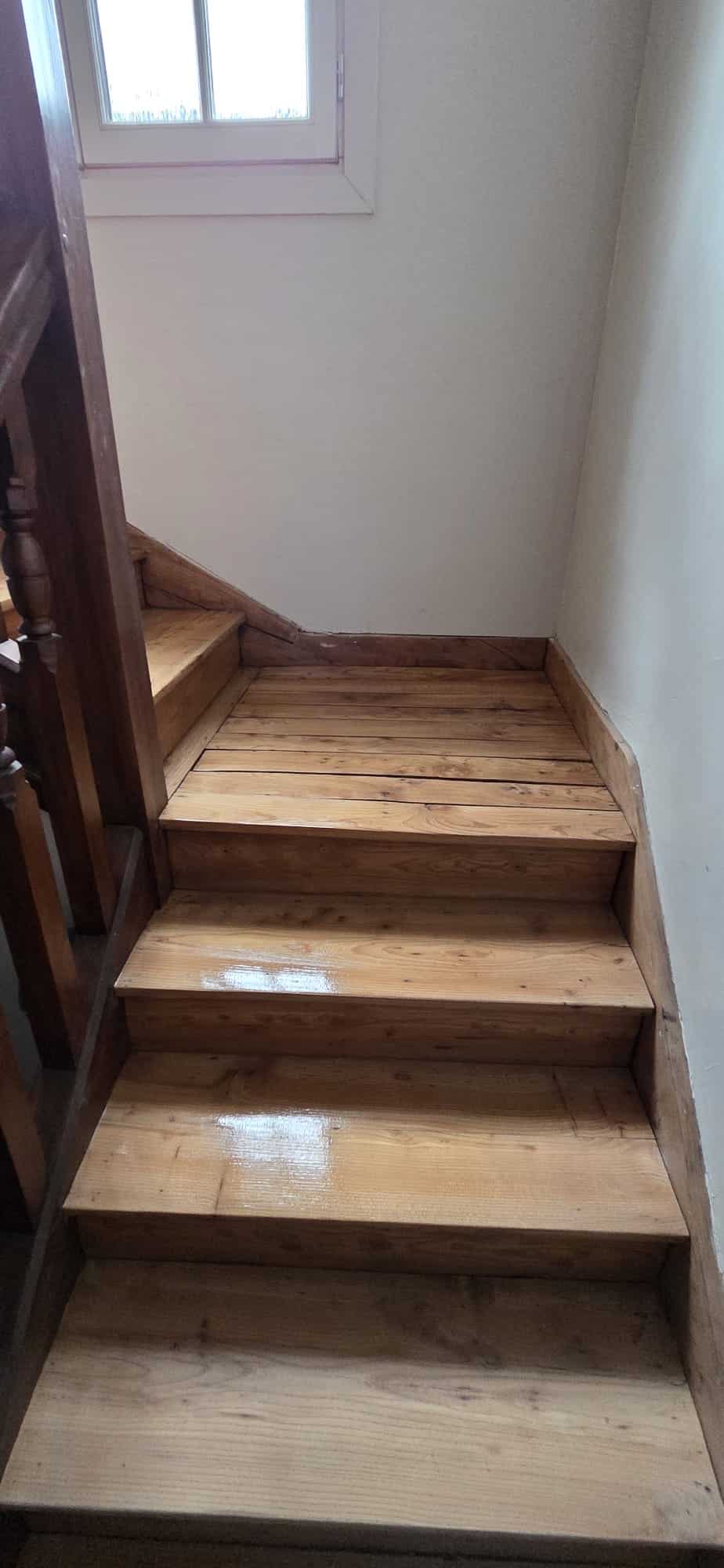 Escalier intérieur en bois de pin verni menant à un palier lumineux dans une maison.
