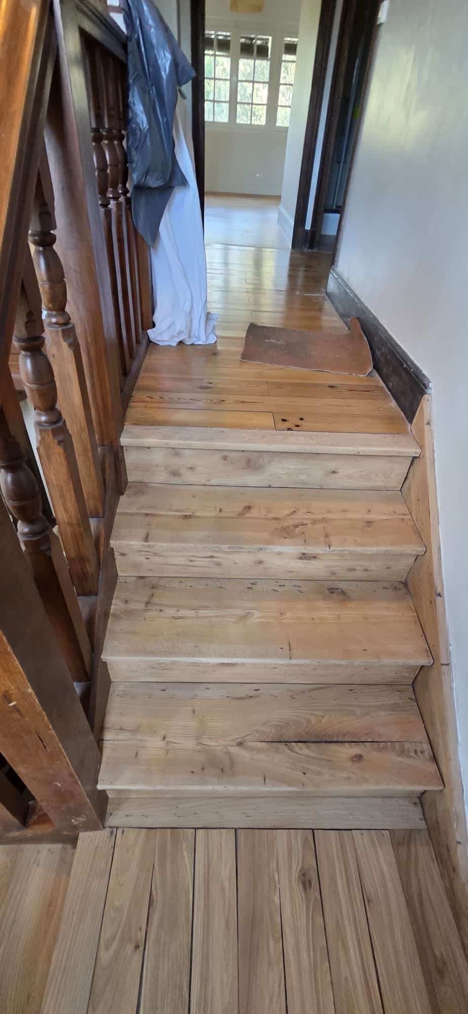 Escalier en bois clair rustique avec rampe sculptée menant à un couloir en parquet de chêne.