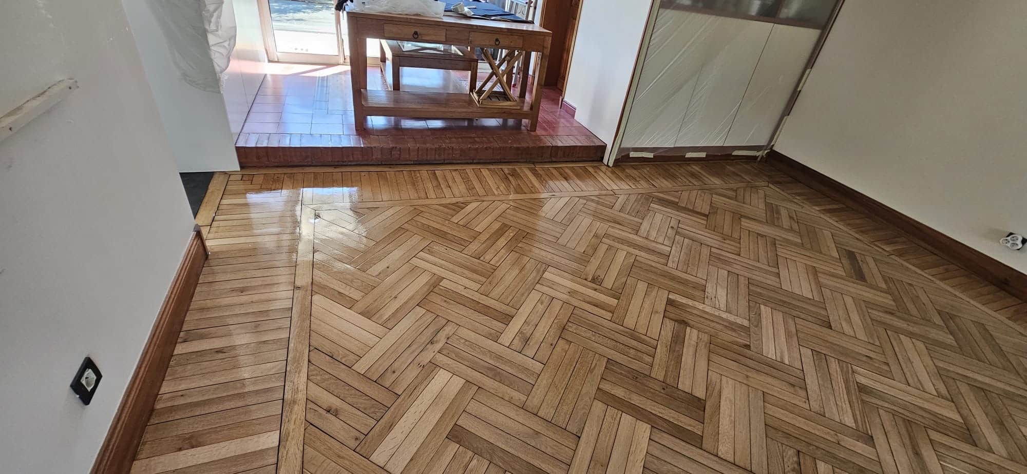 Parquet en bois massif verni avec motif en chevrons croisés dans une pièce lumineuse rénovée.