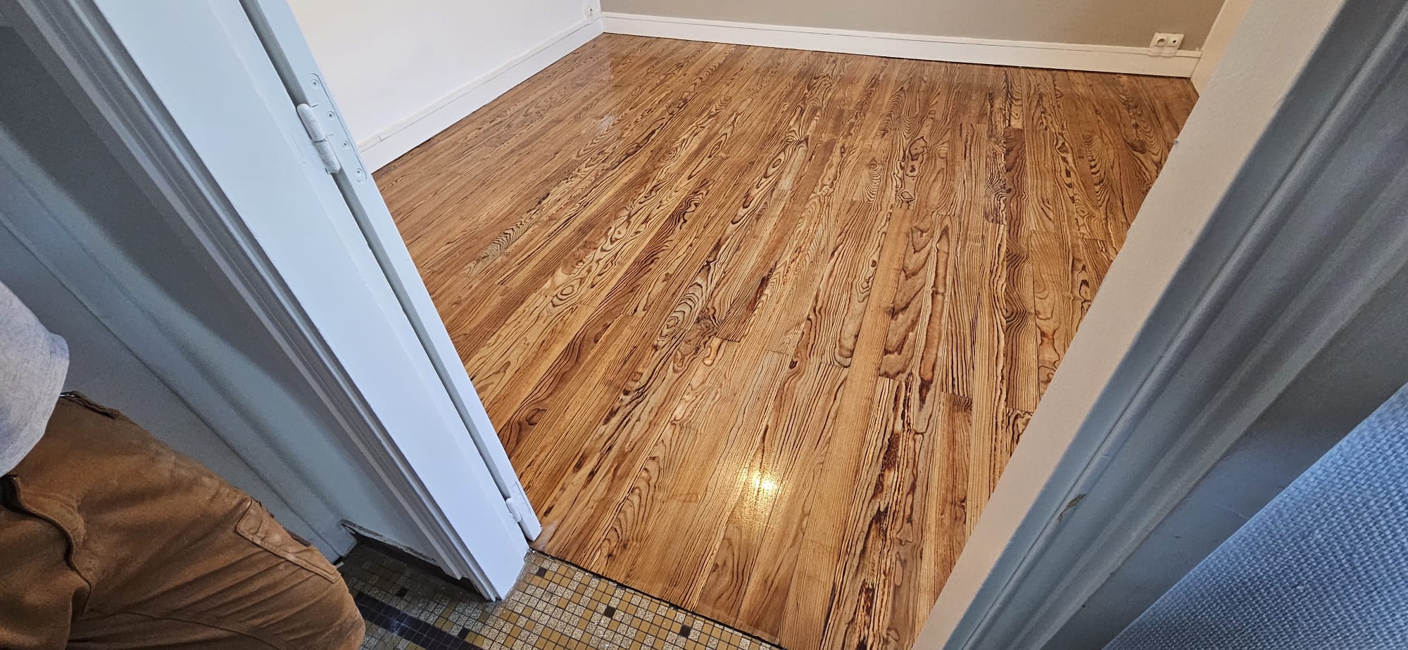 Parquet en bois massif avec grain apparent et finition brillante dans une pièce fraîchement rénovée.