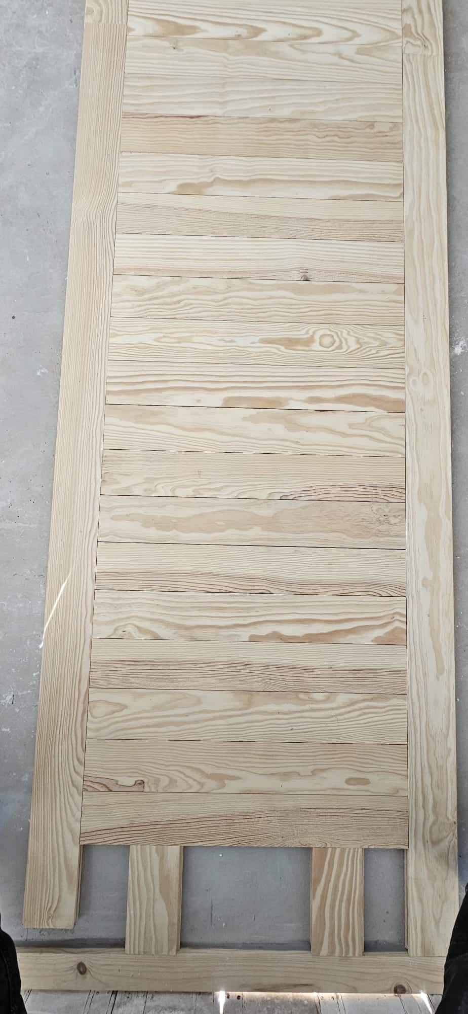 Porte en bois clair de style rustique avec planches horizontales et montants verticaux en cours de fabrication.
