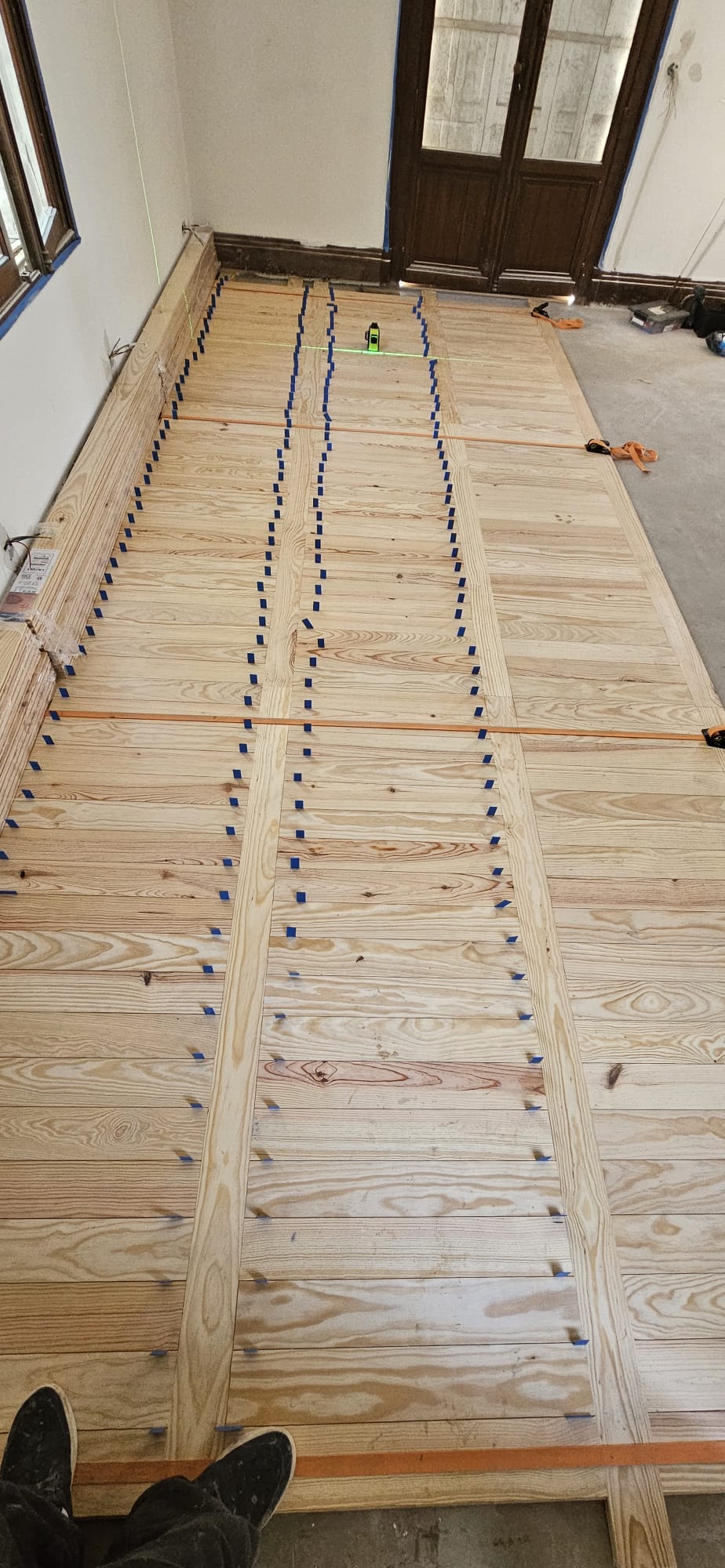 Installation d'un parquet en bois clair avec sangles de serrage et repères bleus pour un motif géométrique précis.
