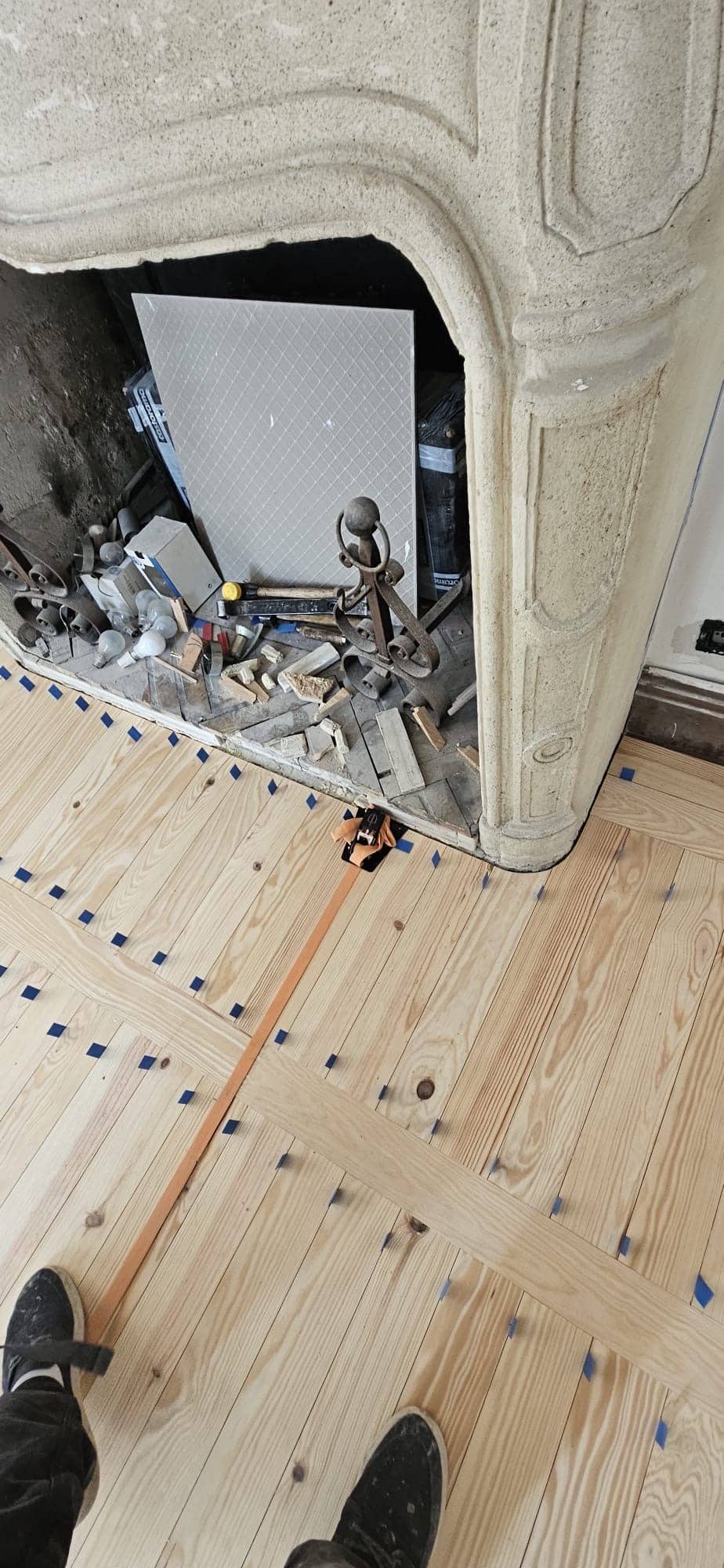 Parquet en bois clair avec croisillons bleus posé devant une cheminée ancienne en pierre en cours de rénovation.