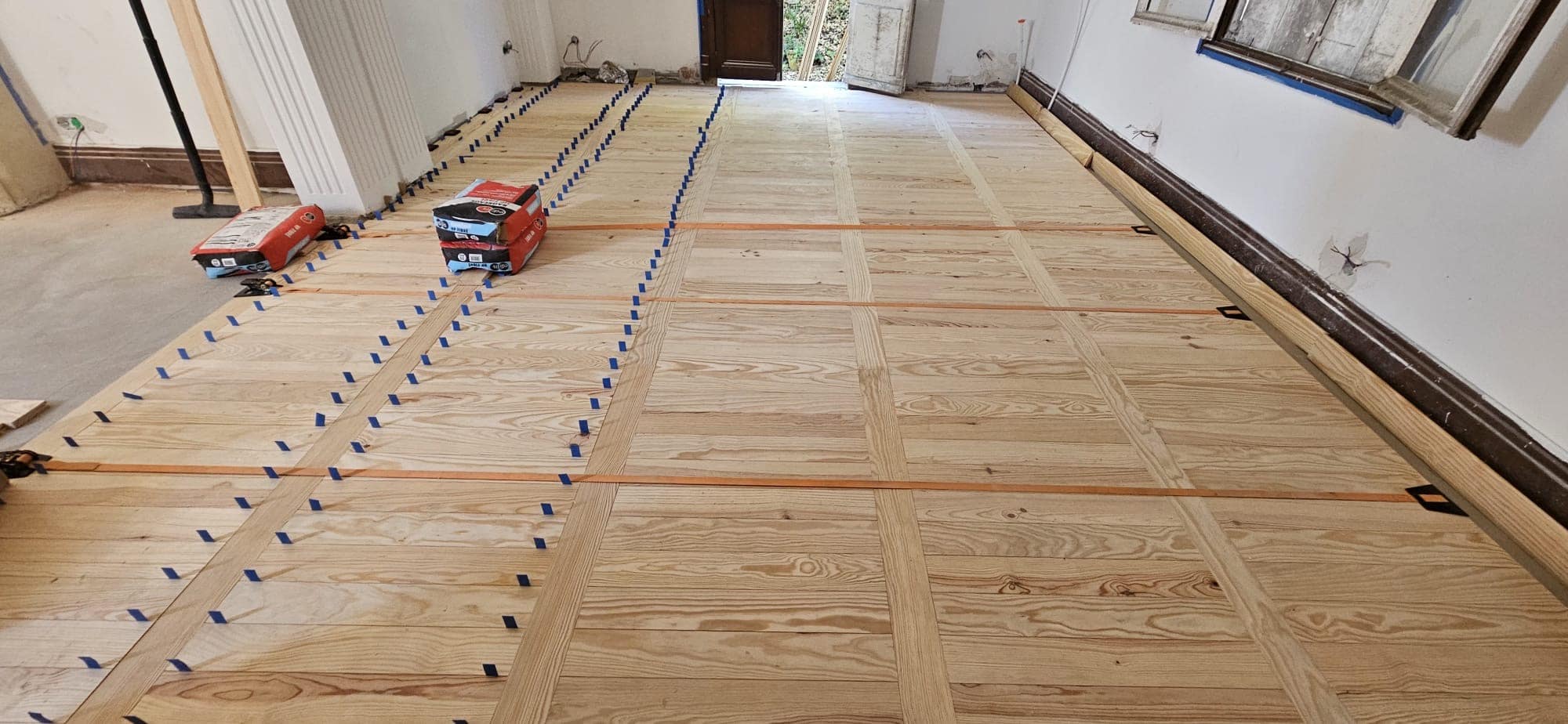 Installation d'un parquet en bois clair avec bandes bleues et sangles de serrage dans une pièce en rénovation.